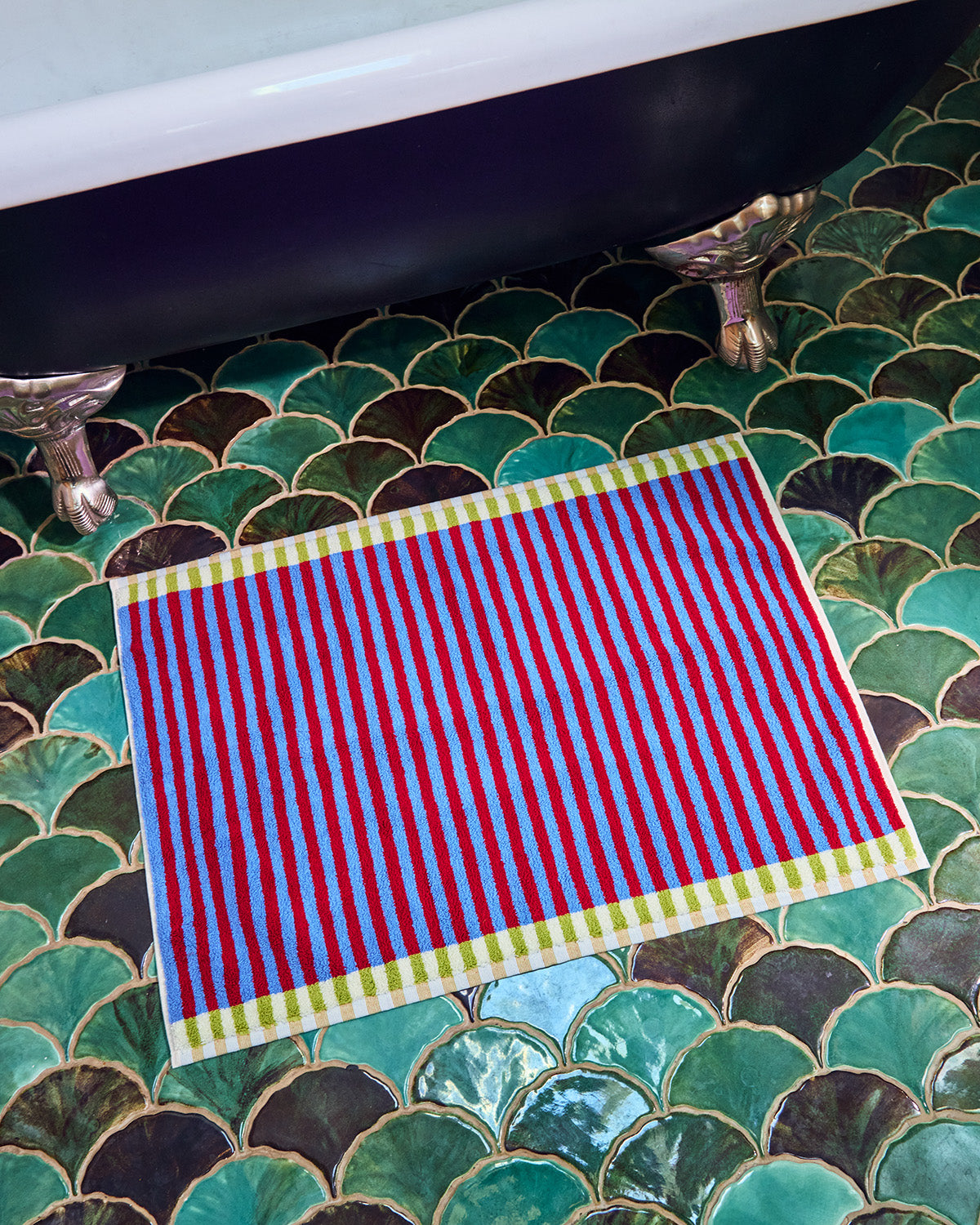 Red and blue striped towel on a green tiled bathroom floor