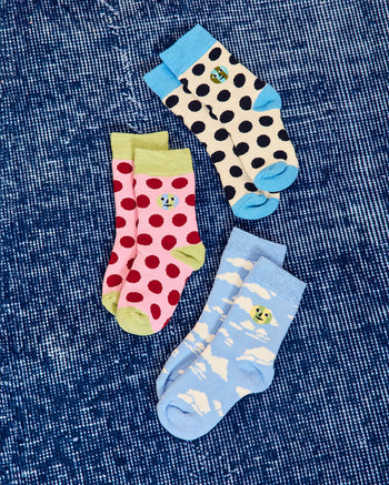 ["Three pairs of patterned baby socks arranged on a blue denim-like fabric background. One pair is cream with black polka dots and bright blue toes/heels, one pair is pink with red polka dots and light green toes/heels. one pair is light blue with white cloud patterns and yellow-green accents. ", "  Wonderful, a sock for every day of the weekend (this only works when it's a long weekend) <br> <br> Model is 4 and wears a size 2-5 yr"]