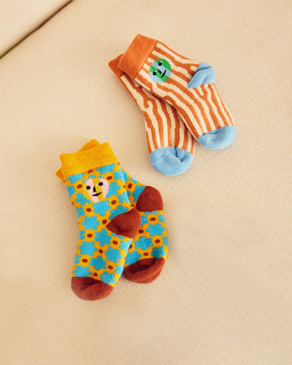 Two pairs of colorful children's socks on a beige surface