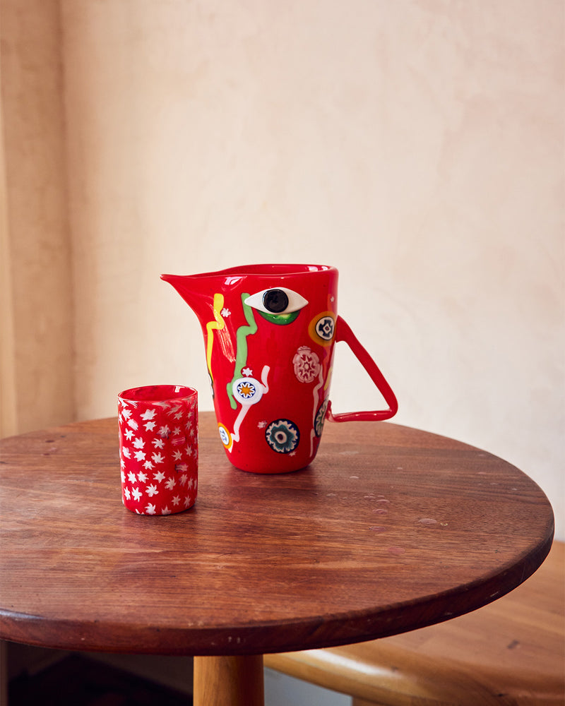Red Murano pitcher with Murrine patterns with matching glass on table