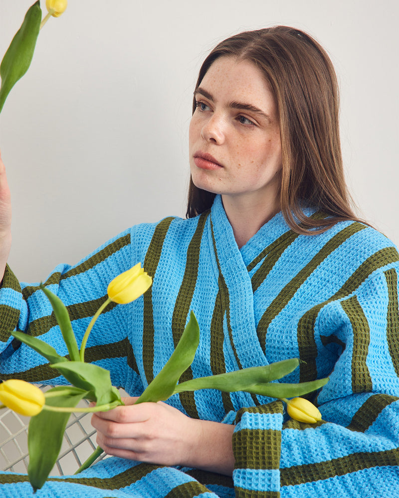 Person wearing a blue and green striped robe holding yellow tulips against a neutral background