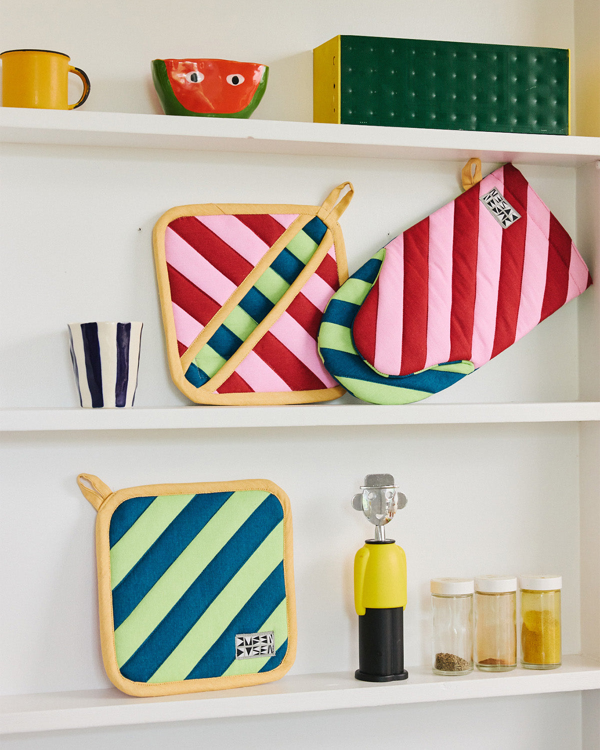Brioche oven mitt and two pot holders on a white kitchen shelf