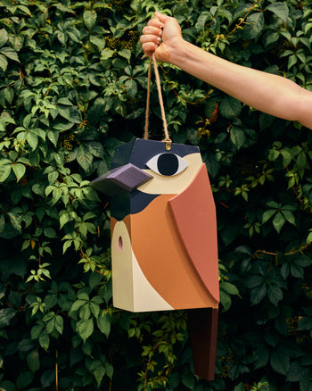 Hand holding a colorful birdhouse against a green leafy background