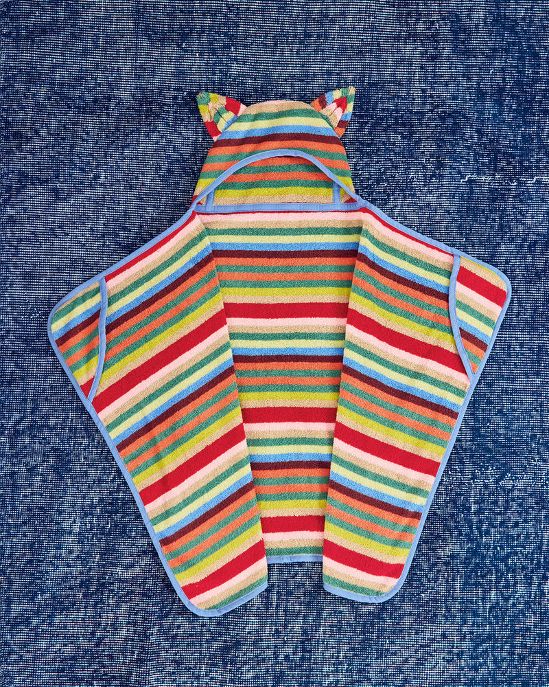 A colorful striped hooded towel laid flat on a blue textured fabric background. The hood has cat-ear details, and the body features horizontal stripes in red, yellow, green, blue, pink, and white, with a light blue border.