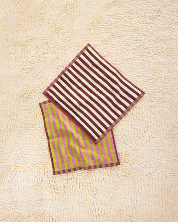 Two striped towels, one red and white, one green and pink, on a textured beige surface. 