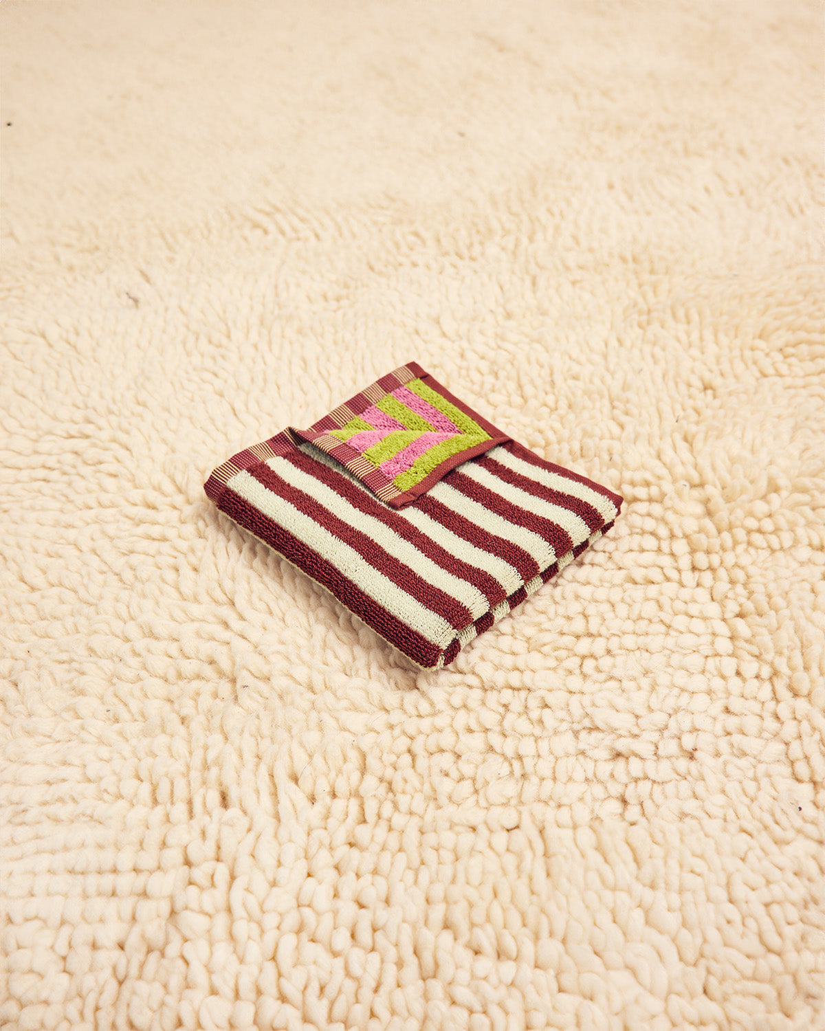 Caterpillar washcloth in maroon, white, pink, and green folded on beige carpet