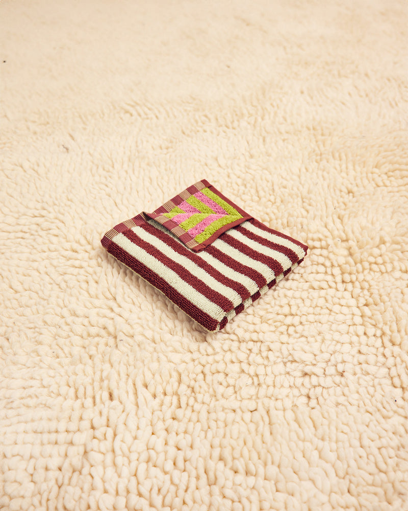 Caterpillar washcloth in maroon, white, pink, and green folded on beige carpet