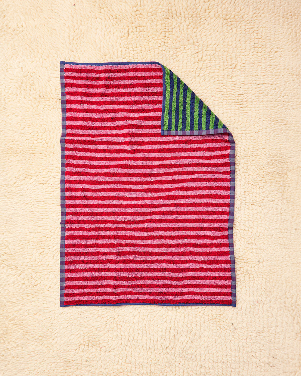 Green and blue striped towel with red and pink overside on beige rug