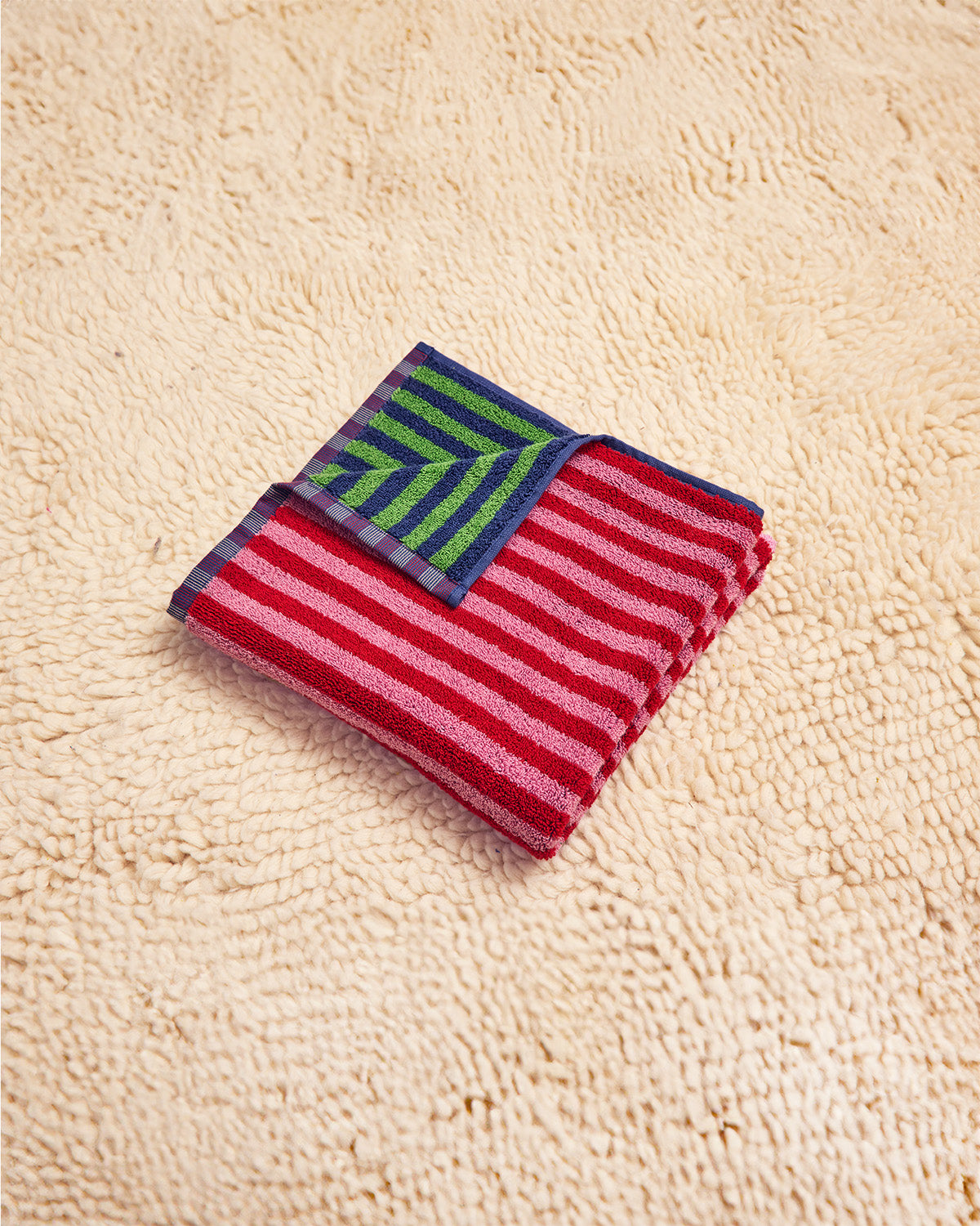 Green and blue striped towel with red and pink overside folded on beige rug