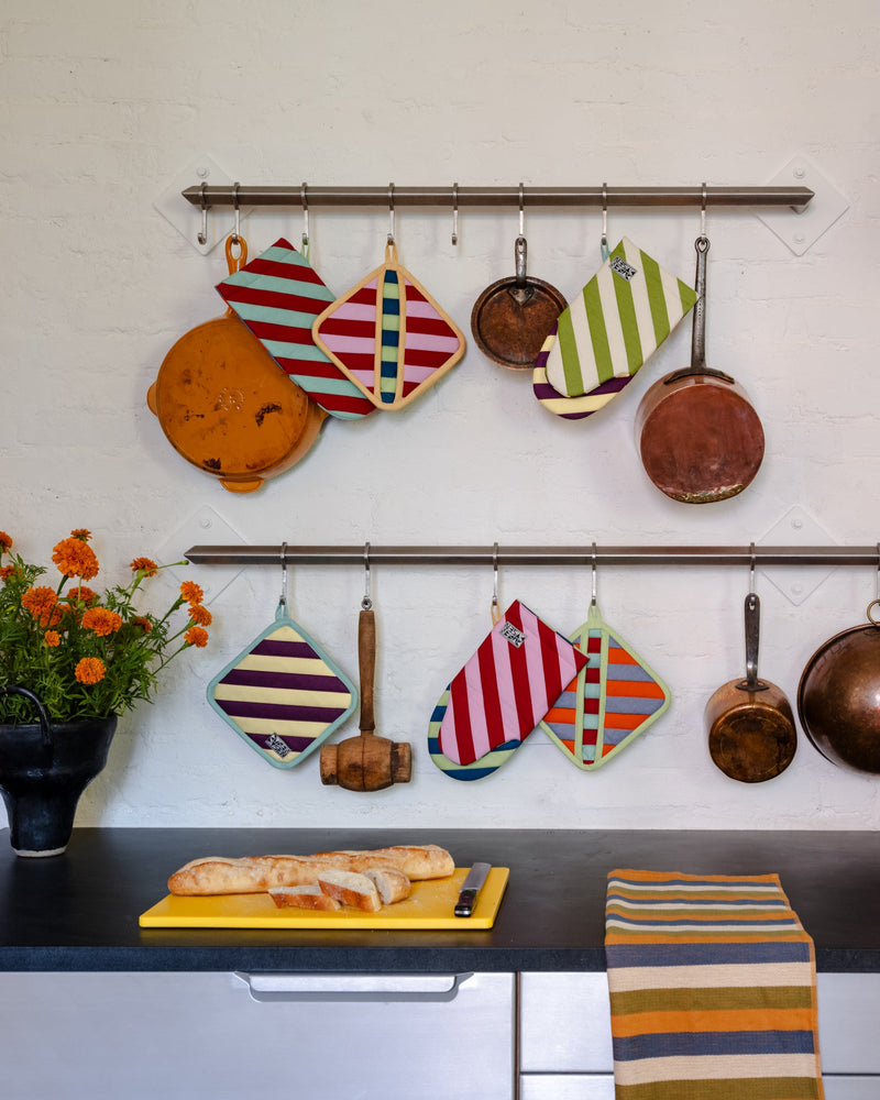 Kitchen wall with hanging pots, pans, and colorful oven mitts on a white tiled wall.