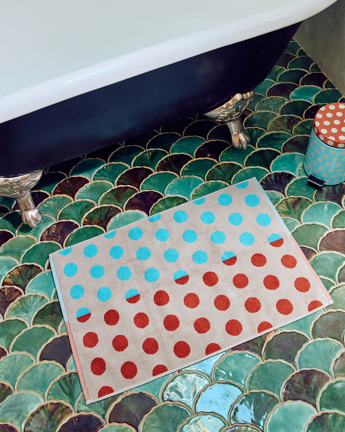 Bath mat with red and blue polka dots on a green tiled bathroom floor.