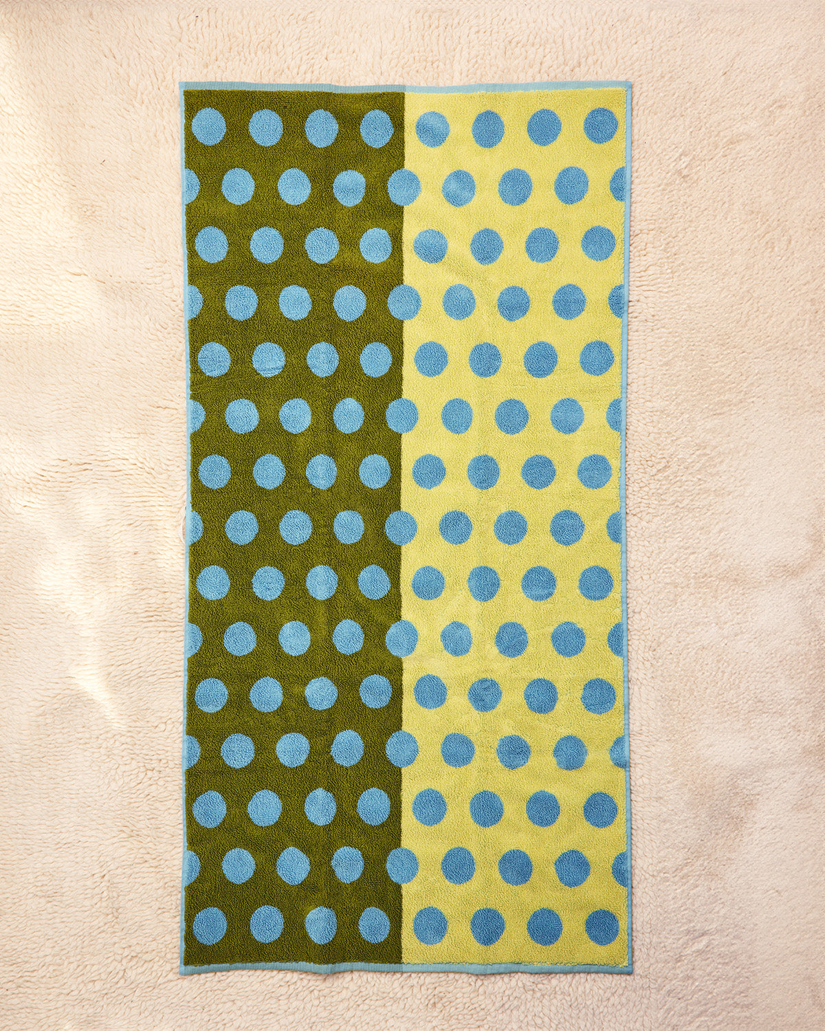 Towel with green and yellow stripes and blue polka dots on a beige background