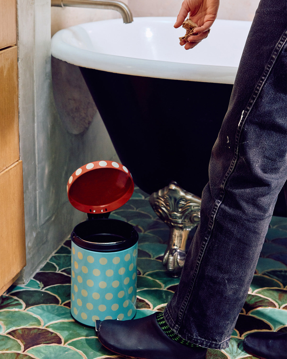 Person using a portable trash can with a polka dot design in a bathroom setting.
