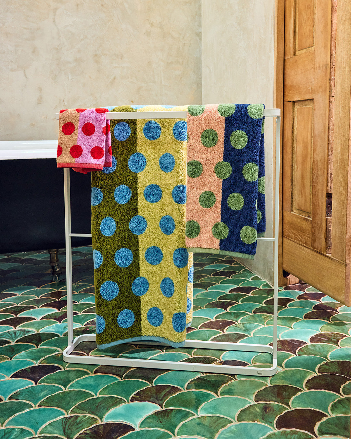 Colorful polka dot towels on a metal towel rack against a tiled bathroom wall. 