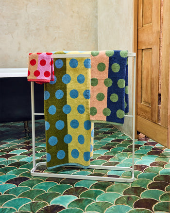Colorful polka dot towels on a metal towel rack against a tiled bathroom wall. 