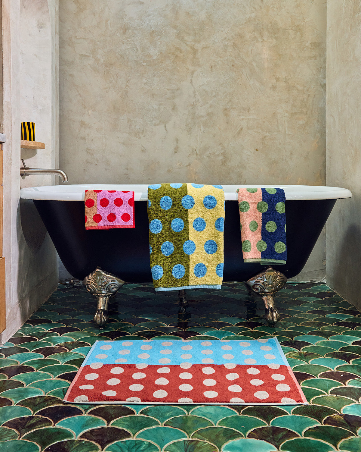 Bathroom with a black freestanding bathtub decorated with colorful polka dot towels on a patterned green and blue tiled floor. ; If you really want to drive your point home