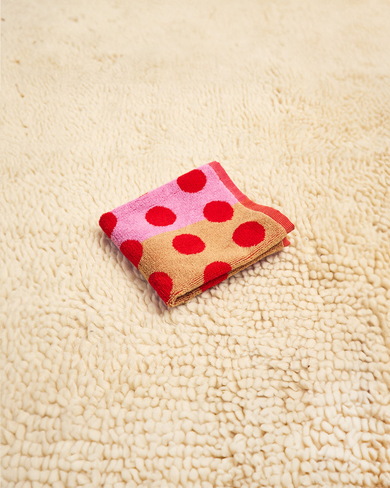 Folded washcloth with red polka dots on a beige carpet