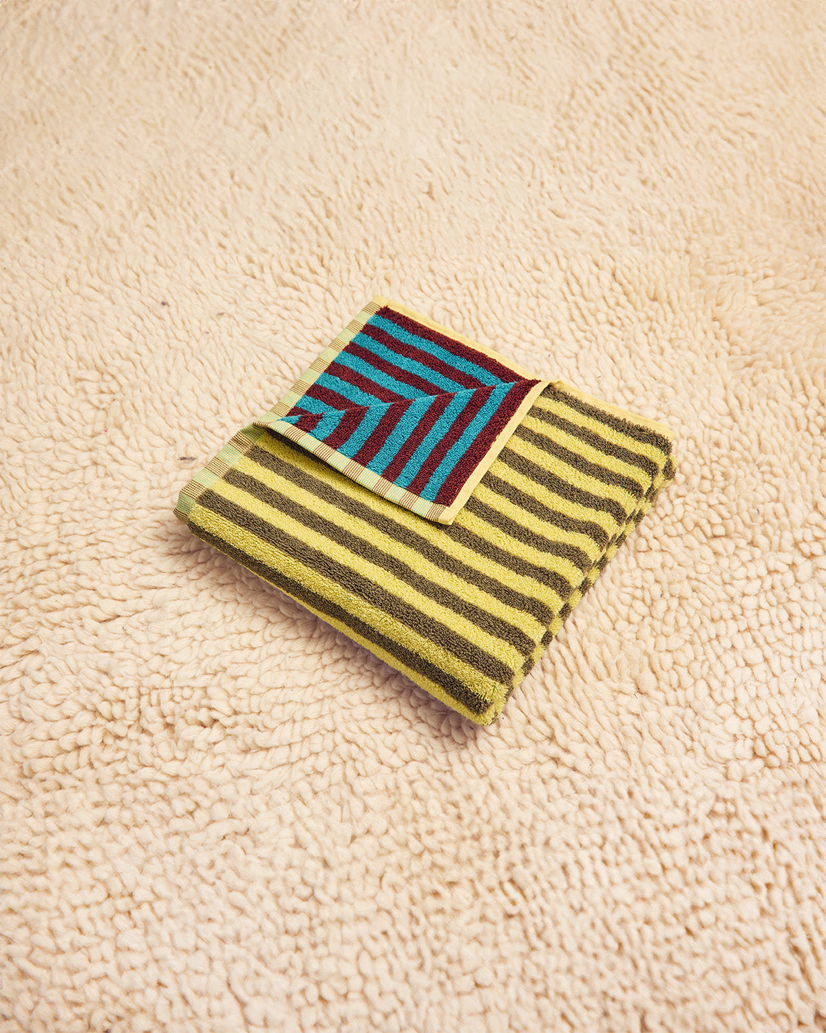 Dragonfly towel in yellow, beige, maroon and blue folded on beige carpet