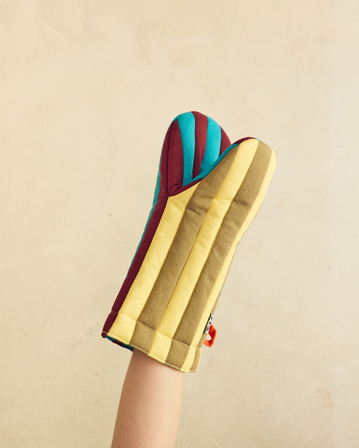 Colorful oven mitt with gold, blue, and red stripes held by a hand against a beige background