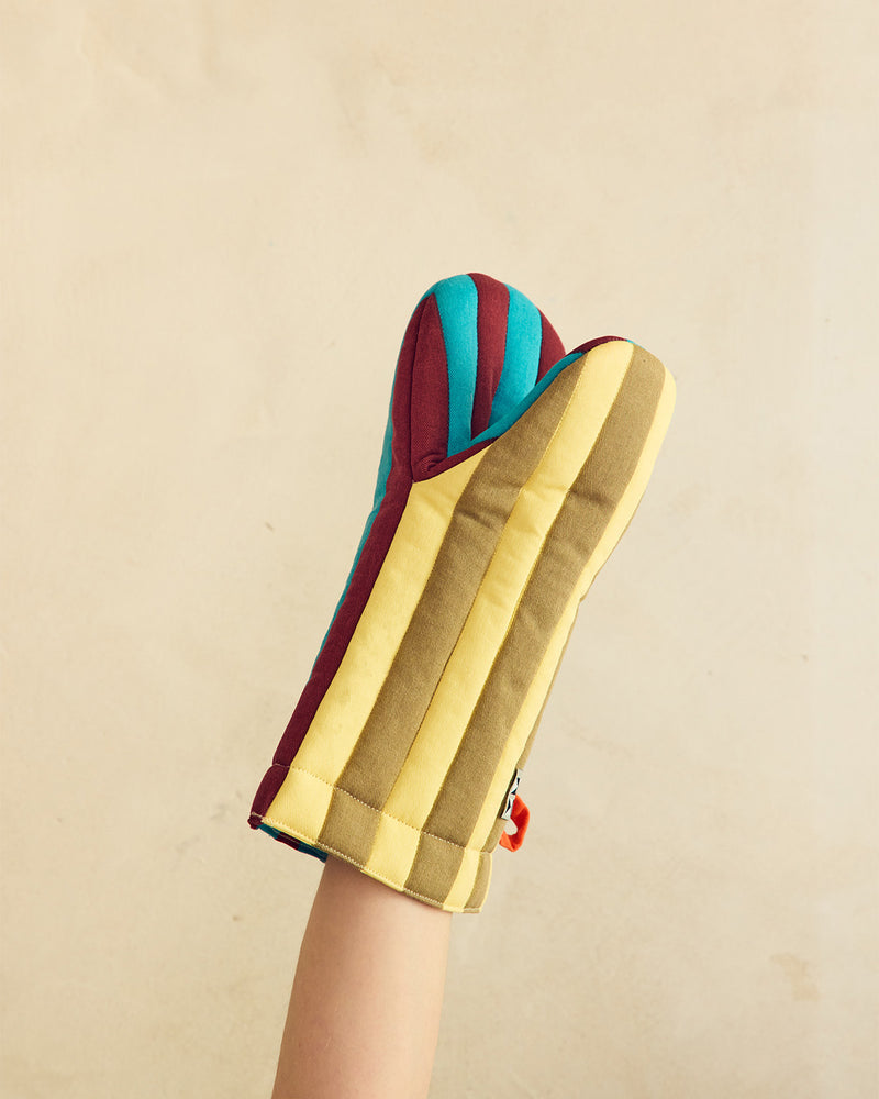 Colorful oven mitt with gold, blue, and red stripes held by a hand against a beige background
