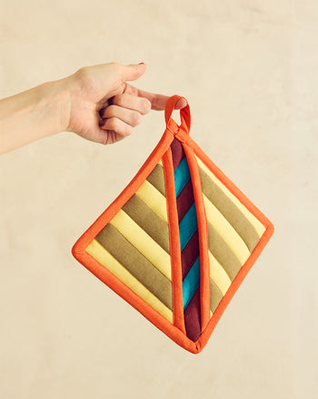 Hand holding a colorful striped pot holder against a beige background