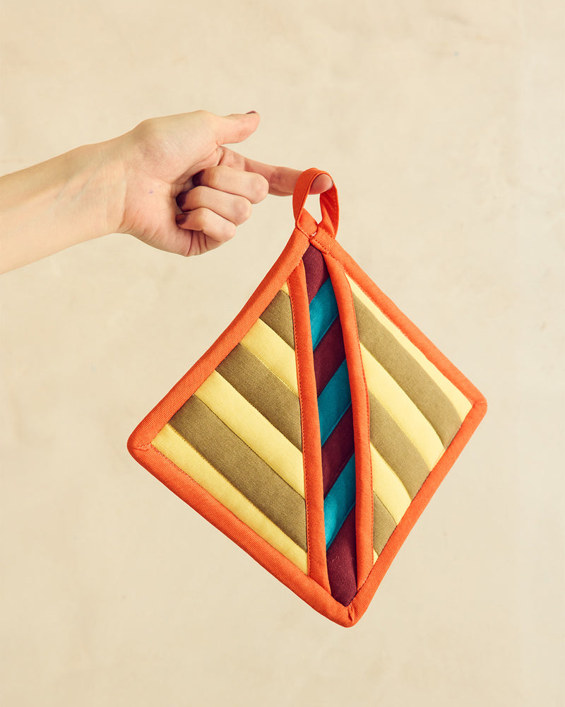 Hand holding a colorful striped pot holder against a beige background