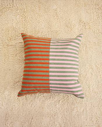 ["A square throw pillow with a split design, featuring orange and sage green stripes on the left half and light pink and sage green stripes on the right half, displayed on a textured beige rug. ", " Go Dutch on your couch design"]
