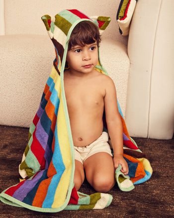 Child wearing a colorful striped towel with animal ears, sitting on the floor. 