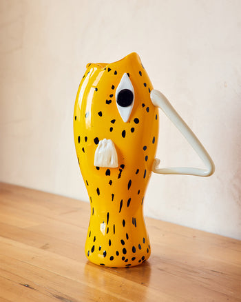Murano Glass Yellow vase with black spots and a white handle on a wooden surface. Shaped like a fish 