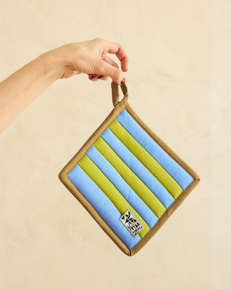 Hand holding a striped pouch with blue and green stripes on a beige background