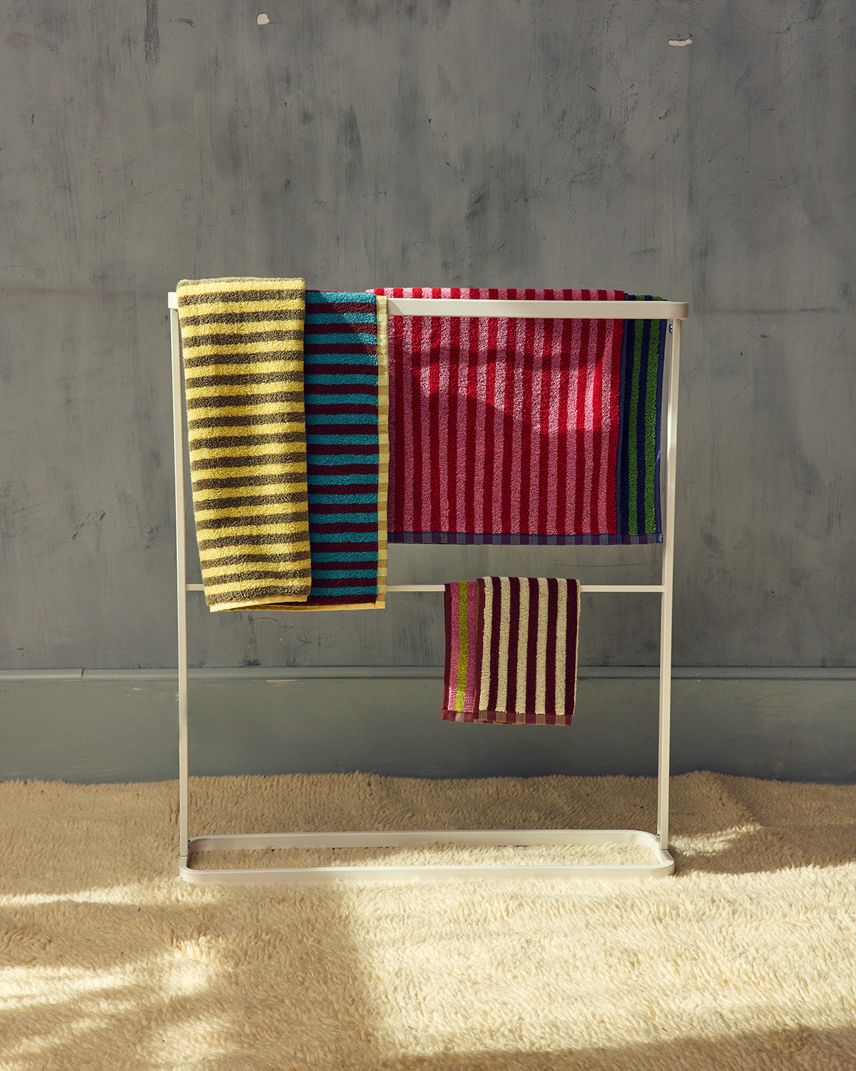 Colorful striped towels on a metal rack against a gray wall. 