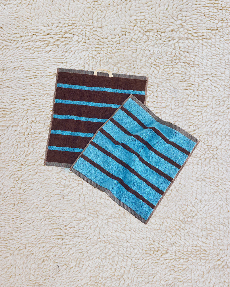 Two striped cloths, one brown and blue, the other blue and gray, on a textured beige surface.