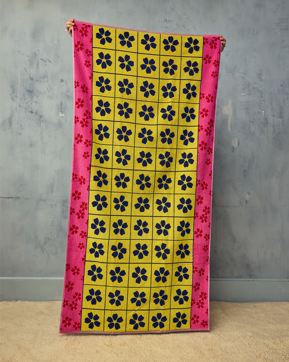 Colorful towel with floral pattern held against a gray wall