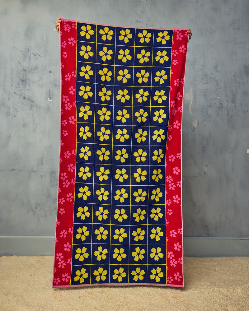 Towel with yellow floral pattern on a blue background, held against a gray wall.