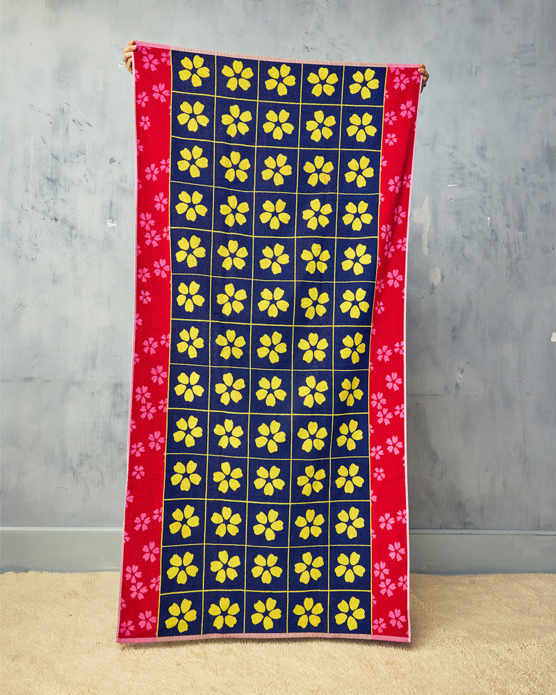 Towel with yellow floral pattern on a blue background, held against a gray wall.