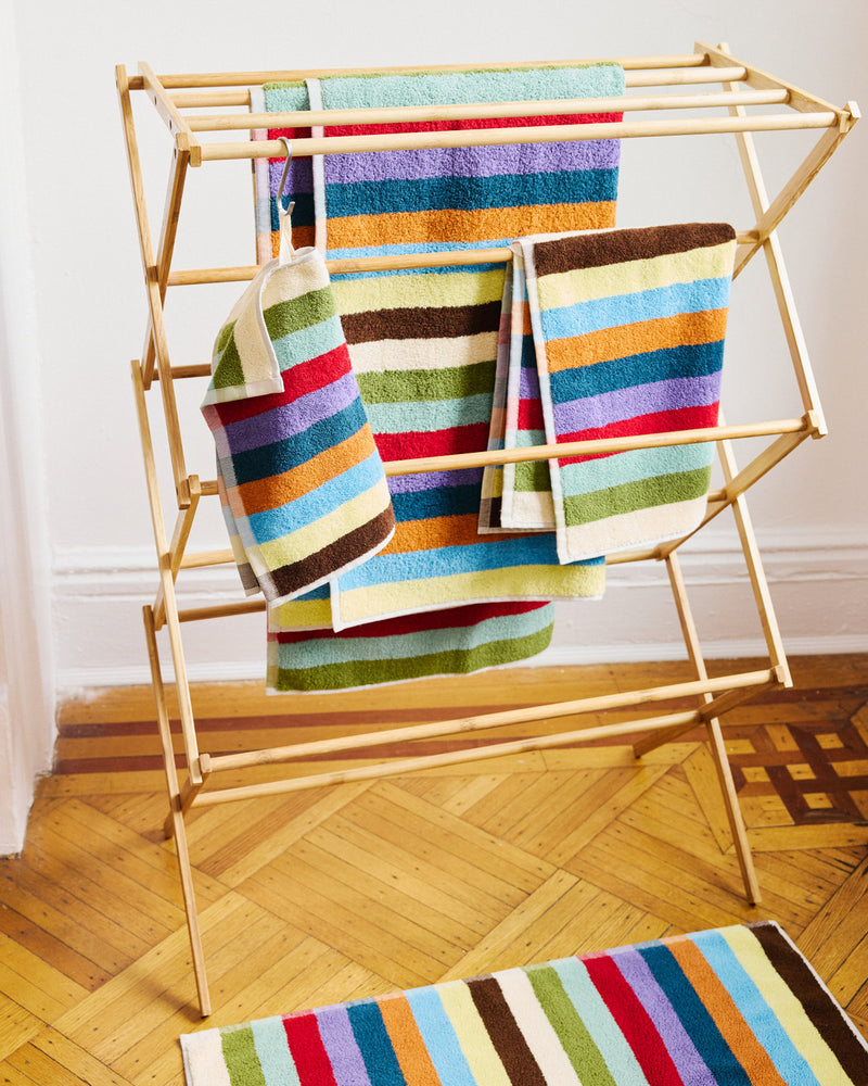 Colorful striped towels on a wooden drying rack with a matching bath mat on the floor.