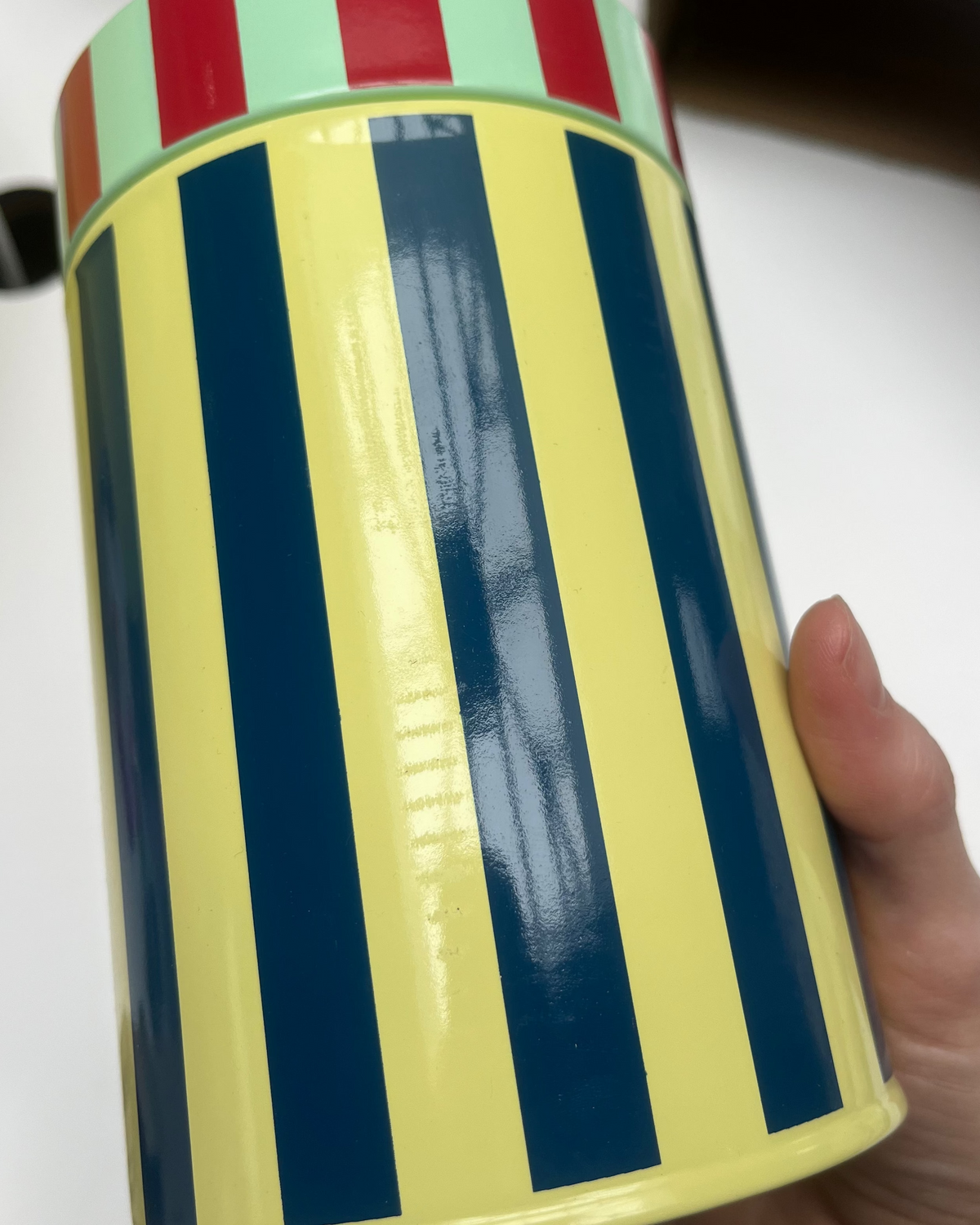 Colorful striped container held by a hand on a white surface