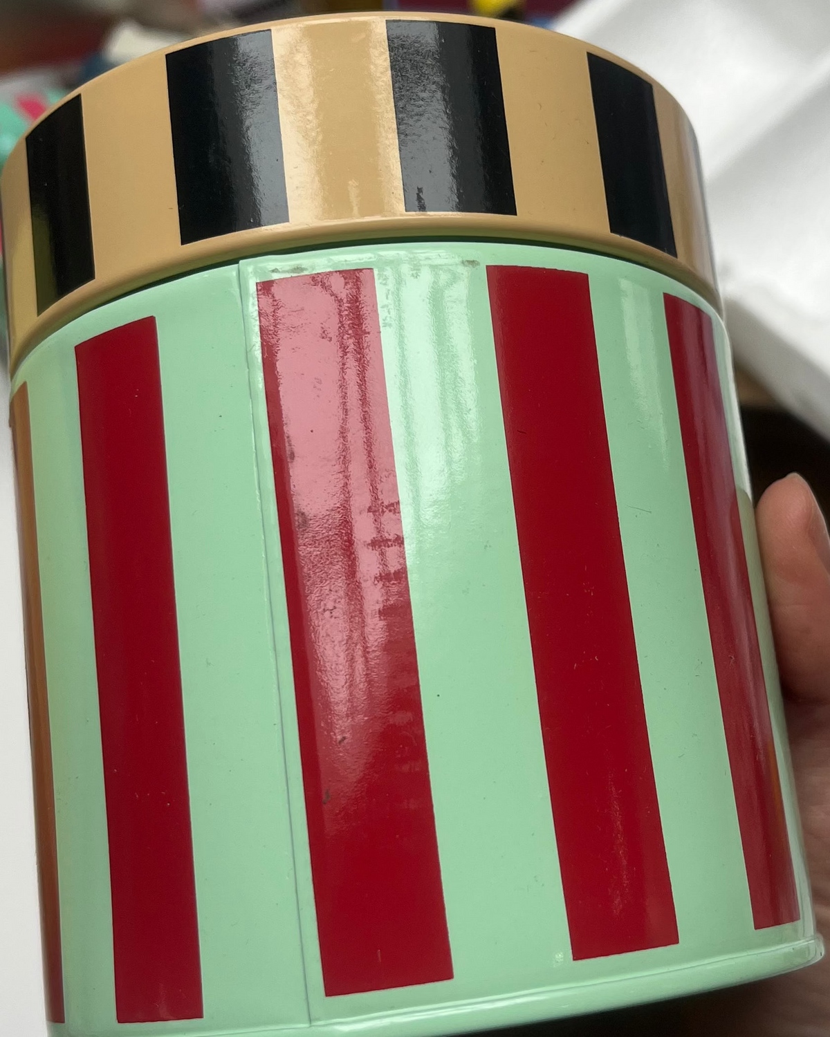 Hand holding a cylindrical container with red and green stripes on a blurred background