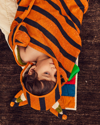 Child wearing an orange and black striped hooded towel on a brown rug 