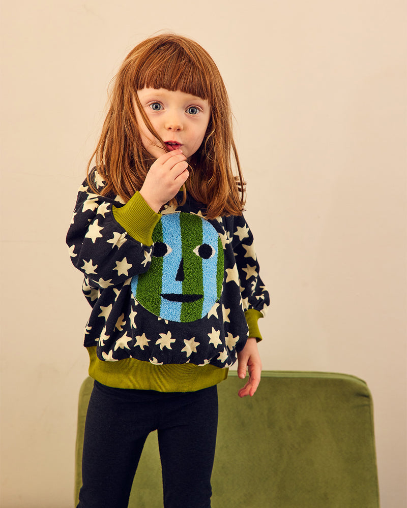 girl in star sweatshirt with smiley face on front on green chair