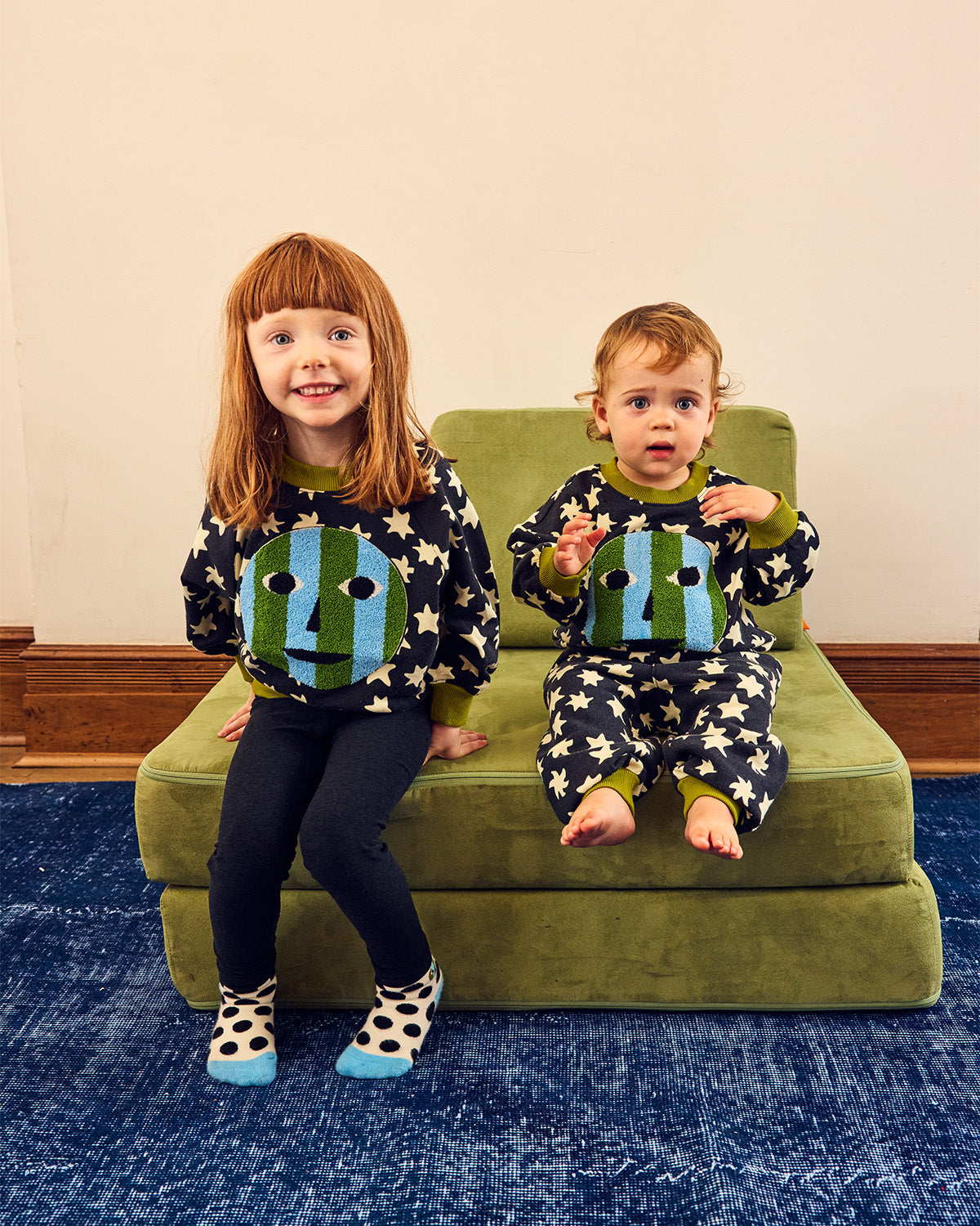 girl and baby in matching sweatshirts on green chair on blue rug