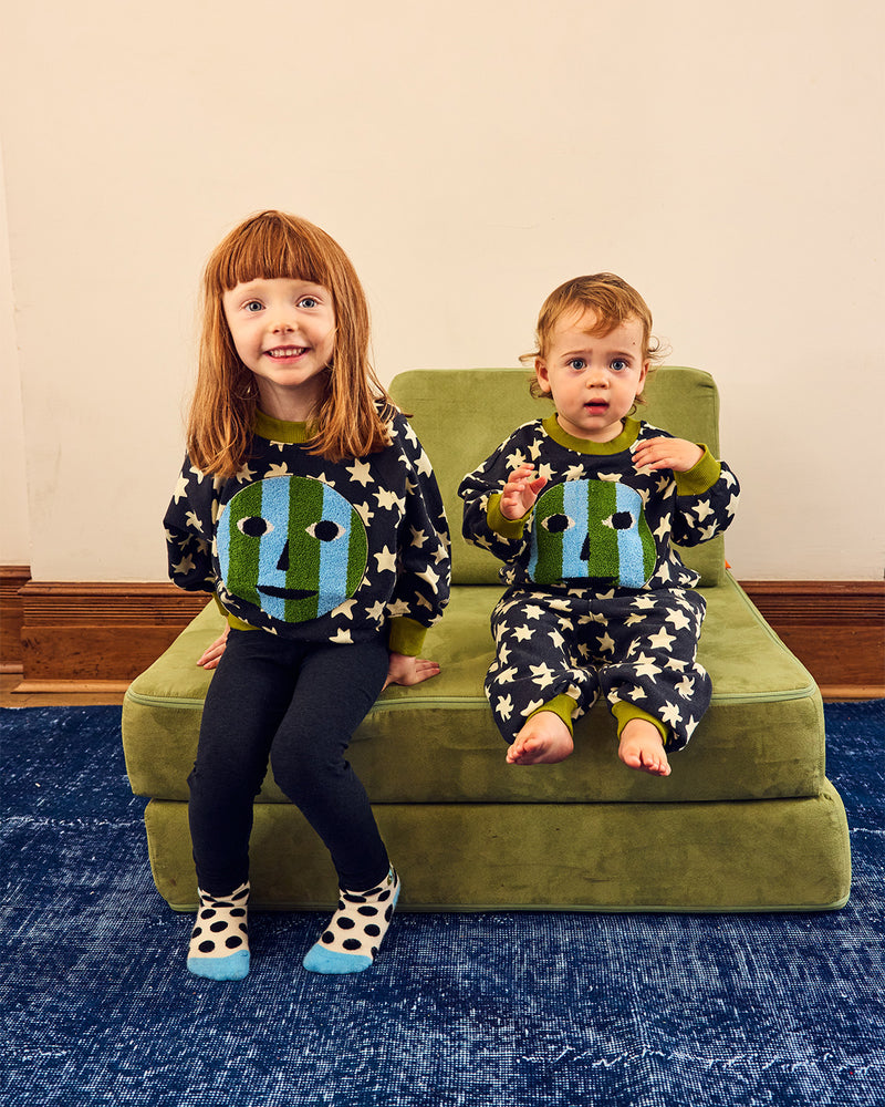 girl and baby in matching sweatshirts on green chair on blue rug