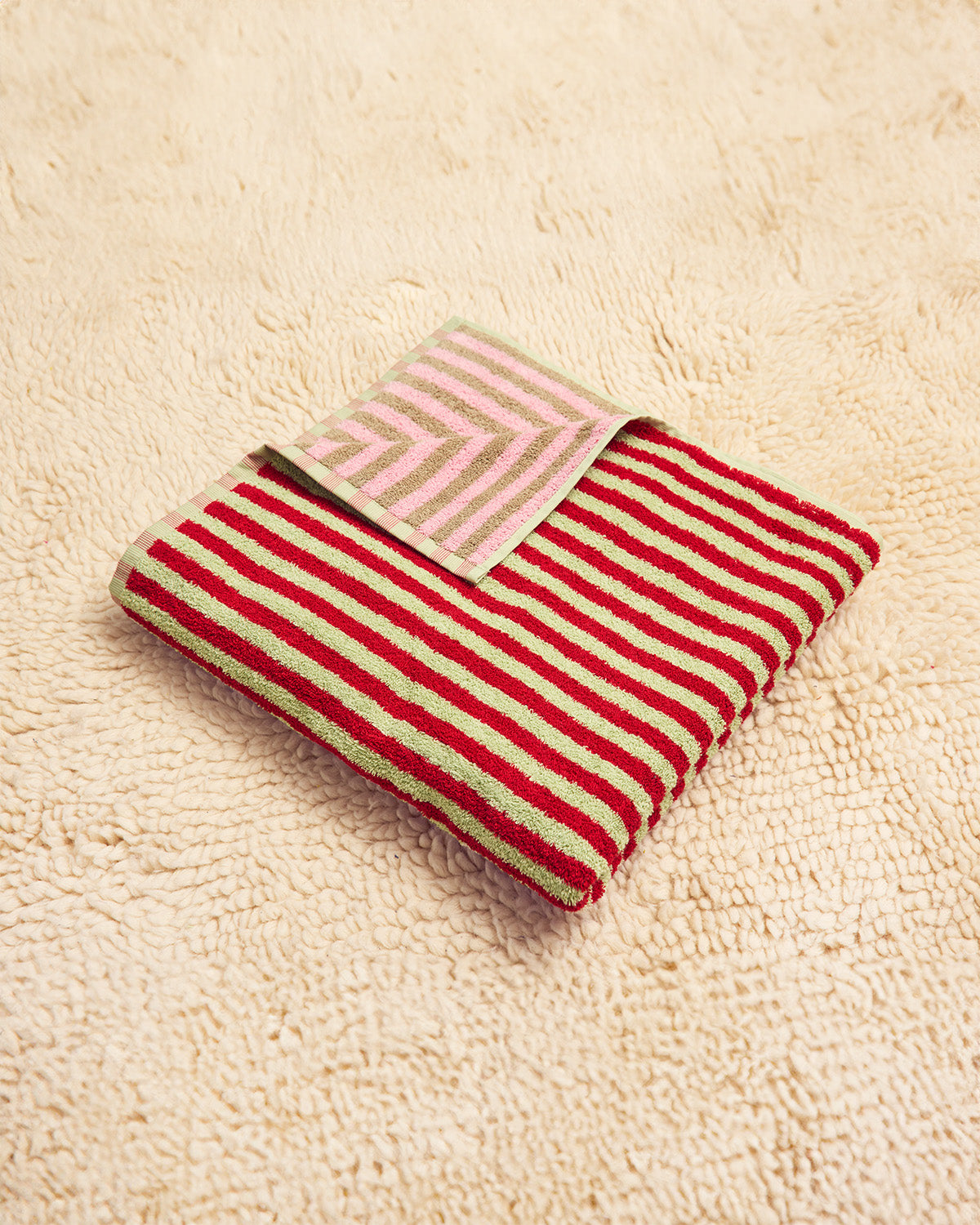 Red and green striped towel on a beige textured surface with pink and taupe on other side