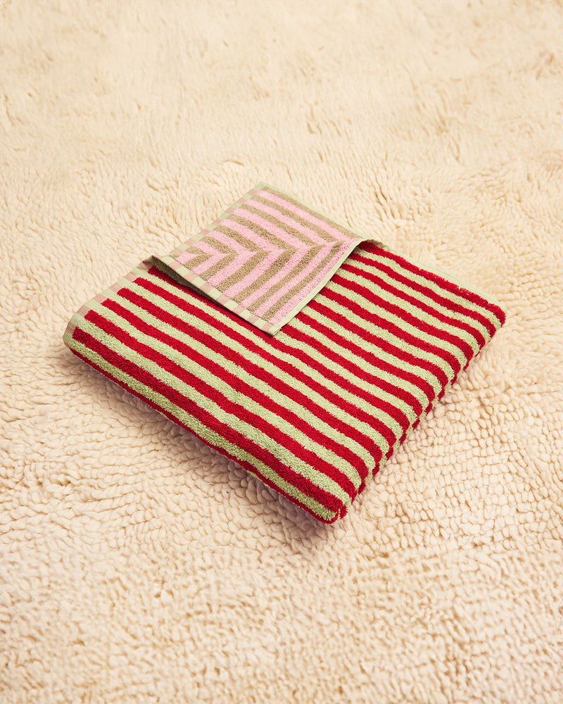 Red and green striped towel on a beige textured surface with pink and taupe on other side