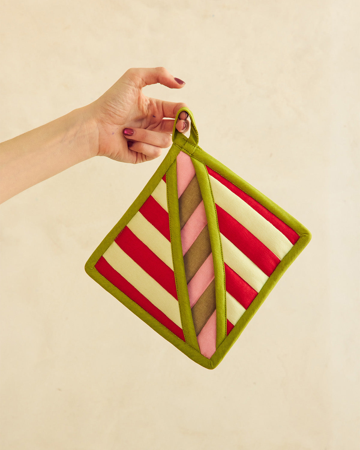 Hand holding a striped pot holder with a green border on a beige background