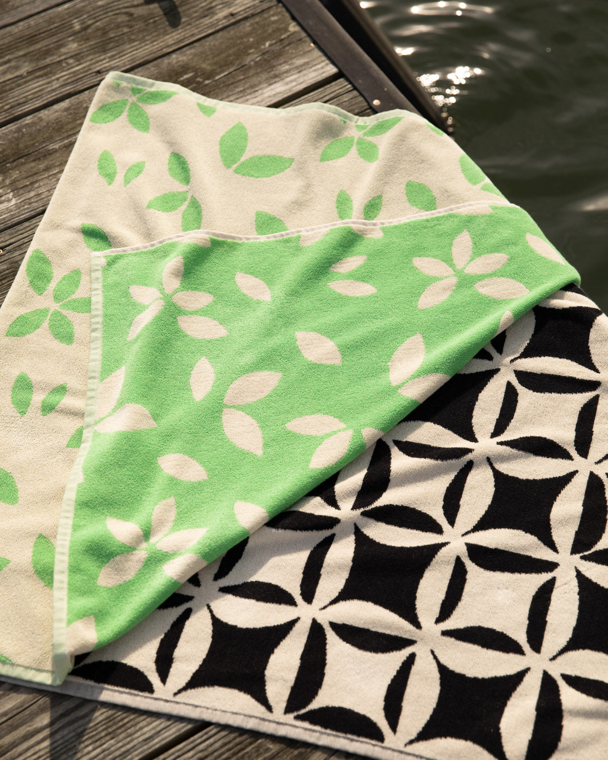 Green and white patterned towel on a wooden surface with water in the background
