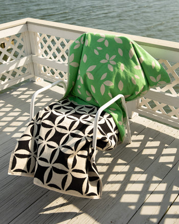 Two patterned towels draped over a chair on a wooden deck by a body of water. 