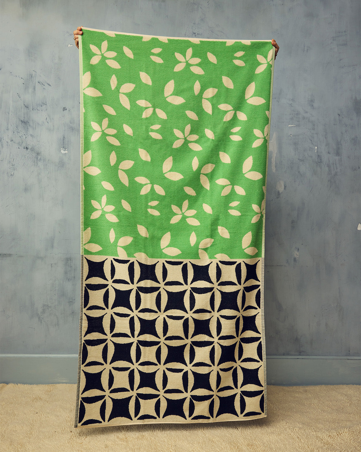 Green and black patterned fabric draped over a wooden rod against a gray wall.