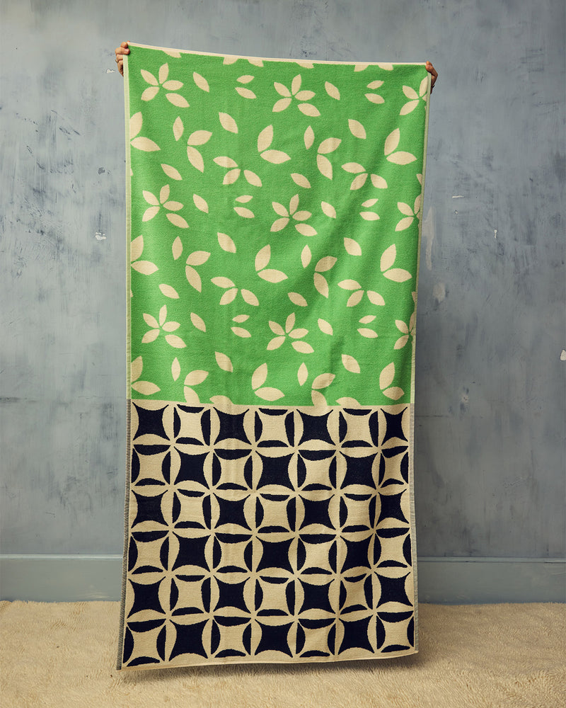 Green and black patterned fabric draped over a wooden rod against a gray wall.