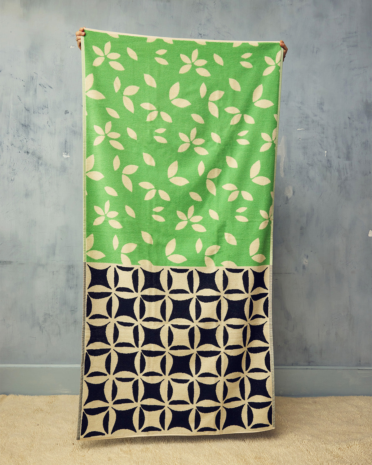 Green and black patterned beach towel against a gray wall.